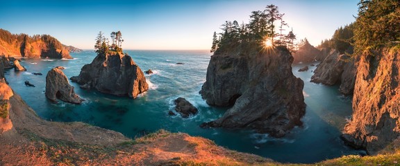 Sunset at Natural Bridges along Samuel H. Boardman State Scenic Corridor, Oregon during a golden hour - sunbeams through trees with dense vegetation. Beautiful seascape with rocks. West Coast USA