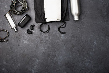Towel, bottle of water, charger, air headphones in the gym on the floor. Concept for a sports project. Horizontal. Copy space. Grunge, monochrome,