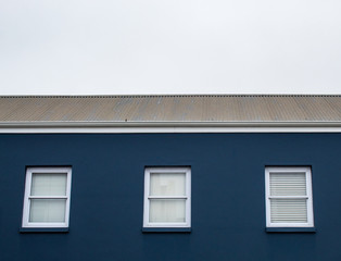 A game of tones and geometries: blue house, white windows, grey sky