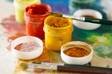 Brushes for drawing and several open jars of gouache of different colors are left on the palette
