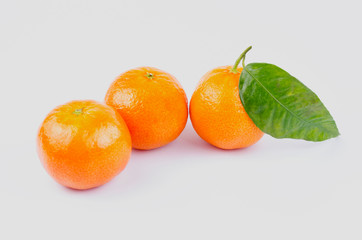 Three ripe tangerines with leaves on a white background