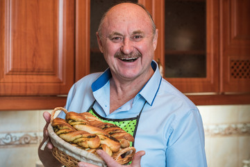 Happy smiling senior man on a kitchen with basket of bread, hobby and good mood in pensioner life 