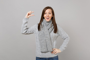 Excited woman in gray sweater scarf gesturing demonstrating size with copy space isolated on grey background. Healthy fashion lifestyle people sincere emotions cold season concept. Mock up copy space.