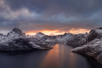 Winter dramatic landscape with snowy mountains, sea, blue and orange cloudy sky reflected in water at sunset. Beautiful Lofoten islands, Norway. Norwegian fjords background. Christmas time concept