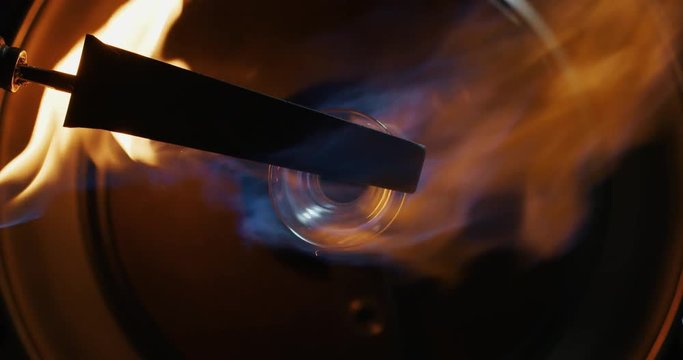 Slow motion macro of glass blower working with flame on a handmade art piece of glass from precious crystal in a workshop. 