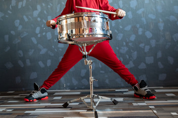 Teen boy in red suit playing drum in room. child holds drumsticks