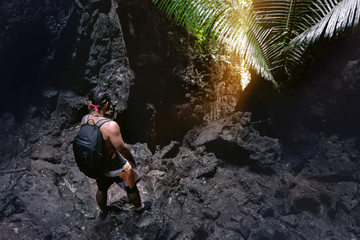 Man climber stands near cave's exit or big rock in darkness