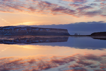 Black sand beach and the mount Reynisfjall, Vik, South Iceland in winter or summer. Panoramic landscape of volcanic mountains and lake in Iceland. Fjord sunset reflection in calm water, dramatic sky