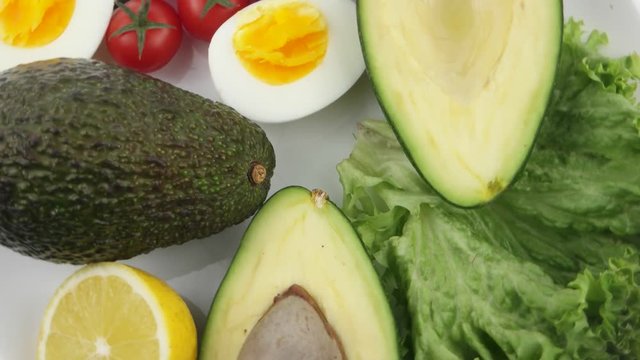 Plate with lettuce leaves, avocado halves, lemon, boiled egg and cherry tomatoes, background