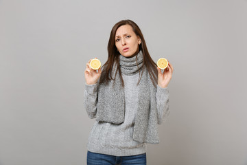 Tired sad young woman in gray sweater, scarf hold lemons isolated on grey wall background, studio portrait. Healthy fashion lifestyle, people sincere emotions, cold season concept. Mock up copy space.