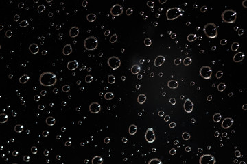 Detail photo - rain water drops behind glass look like bubbles in black liquid. Abstract wet background.