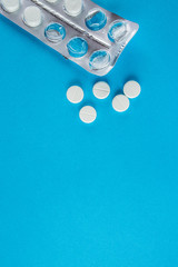 White round pills in pack. Tablets are next to the packaging on a blue background