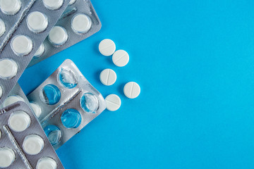 White round pills in pack. Tablets are next to the packaging on a blue background