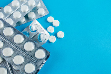 White round pills in pack. Tablets are next to the packaging on a blue background