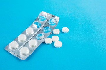 White round pills in pack. Tablets are next to the packaging on a blue background