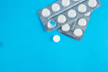 White round pills in pack. Tablets are next to the packaging on a blue background