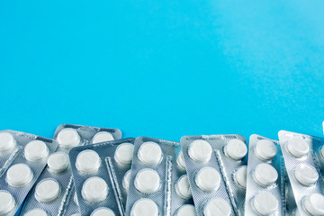 White round pills in pack. Tablets are next to the packaging on a blue background