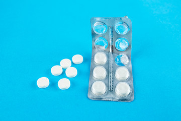 White round pills in pack. Tablets are next to the packaging on a blue background