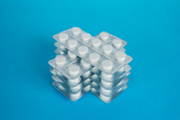 White round pills in pack. Tablets are next to the packaging on a blue background
