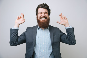 Young bearded successful businessman praying with crossed fingers over gray background