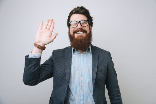 Hi, nice to see you. Friendly-looking attractive bearded businessman waives hand in hello gesture while smiling cheerfully