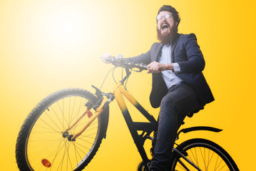 A handsome bearded young man in eyeglasses  and suit riding bicycle on yellow background