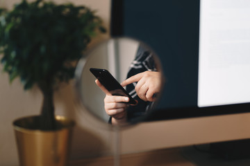 a mirror reflection, creative shot of female hands typing on a cellphone at home.