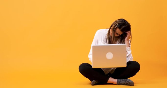 Student girl having an idee while typing on the computer. She is sitting on an yellow background in studio