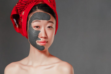 attractive young korean girl with a red towel on her head applied a useful clay mask