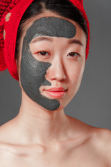 attractive young korean girl with a red towel on her head applied a useful clay mask