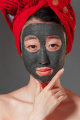 attractive young korean girl with a red towel on her head applied a useful clay mask