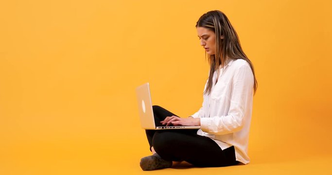 Student sitting on an yellow background and typing fast on computer keyboard