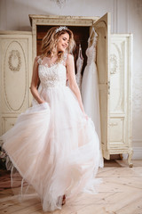 Fototapeta premium Beautiful bride blonde woman sitting near vintage wardrobe full of wedding dresses. fashion beauty portrait 