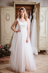Obraz premium Beautiful bride blonde woman sitting near vintage wardrobe full of wedding dresses. fashion beauty portrait 