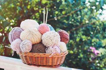 Women's hobby. Skein yarn in a basket and knitting needles in the garden on a Sunny summer day.
