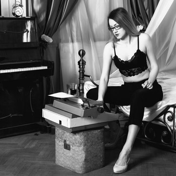 young beautiful woman typing on a retro typewriter. female writer in bra and men's trousers. black and white