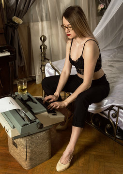 young beautiful woman typing on a retro typewriter. female writer in bra and men's trousers
