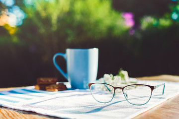 Women's hobby. Crochet and knitting. A blue Cup with a drink, cookies, yarn balls, needles, scissors, knitwear, crochet hooks on a wooden table  in good Sunny weather. The main object out of focus.