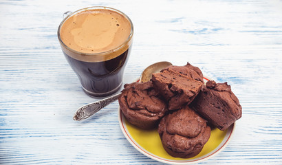 Chocolate muffins and coffee in a glass mug are photographed on a light wooden background.