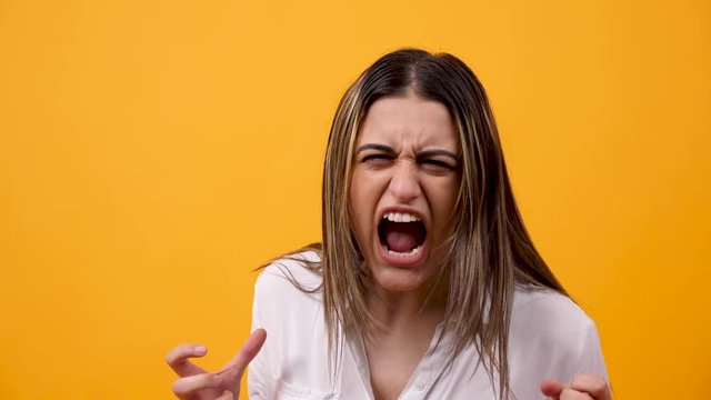 Close up portrait of angry and unhappy woman screaming at the camera on yellow background in studio