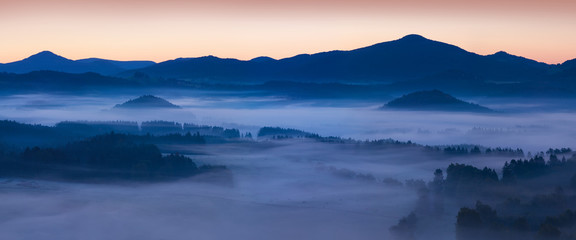 Beautiful summer or autumn sunrise above the forest valley of National park Bohemian Switzerland. Warm sunrise above the deep misty valley. Wonderful landscape background concept. Rays of lights 