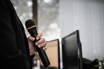 Fototapeta premium Speaker or businessman hold Microphone for speech or speaking in seminar Conference room, talking for lecture to audience university, Computer monitor desk Background. Business Presentation concept
