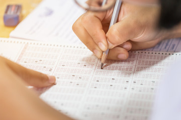 Student taking exams, writing examination on paper answer sheet optical form of standardized test...