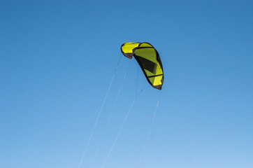 Winter kitesurfing on the frozen sea bay. Bright yellow kite surf on blue sky background, close-up. Sunny clear weather and wind.