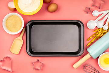 Baking ingredients and empty baking tray on pink background, flat lay