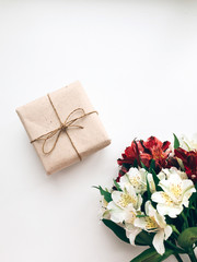 Handmade gift Top view photo Gift box in craft packaging and bouquet of flowers are lying on a white desk