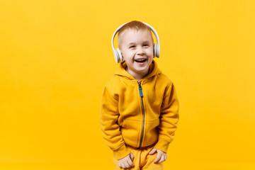 Little kid boy 3-4 years old wearing yellow clothes in headphones isolated on orange wall background, children studio portrait. People sincere emotions, childhood lifestyle concept. Mock up copy space