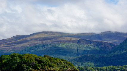 Beautiful hills and mountain peaks covered in trees shrouded in a thick layer of clouds. Irish landscape in County Kerry, Ireland.