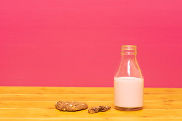 Milk bottle half full of strawberry milkshake with half-eaten cookie