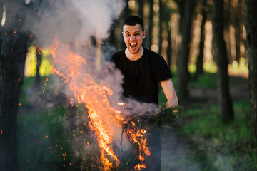 Fototapeta premium Man stands with torches on the background of the forest. An image of man holding burning stick while moving outdoors, surviving in the wild
